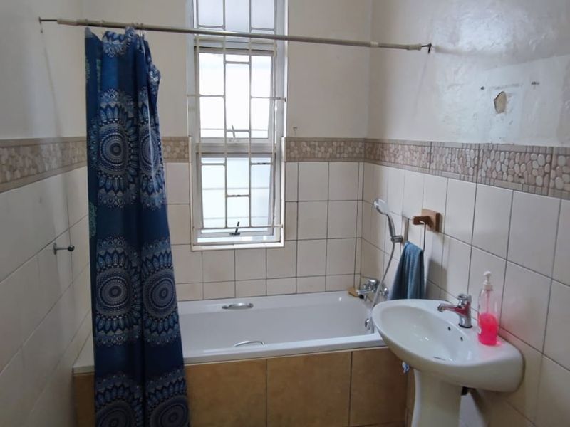 A functional bathroom featuring a bathtub with shower mixer, pedestal basin, and tiled walls with decorative border.