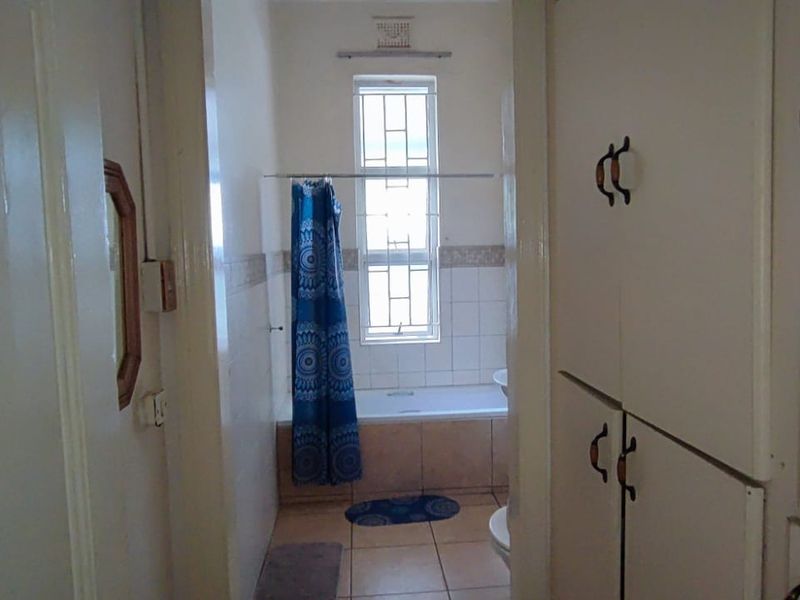 A functional bathroom featuring built-in storage cabinetry, a bathtub with shower curtain, and tiled flooring. The space offers a dated aesthetic ready for modernization.