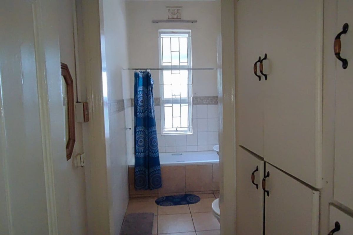 A functional bathroom featuring built-in storage cabinetry, a bathtub with shower curtain, and tiled flooring. The space offers a dated aesthetic ready for modernization.