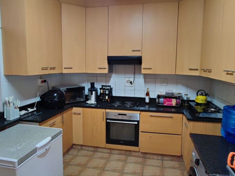 A functional kitchen featuring light wood-finish cabinetry, black granite countertops, integrated oven and hob, and tiled flooring with a tiled backsplash.