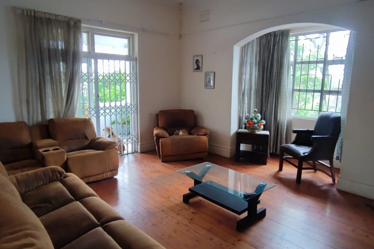 Spacious living room featuring original hardwood flooring, an arched window, and a fireplace mantel, offering a bright and comfortable living space.