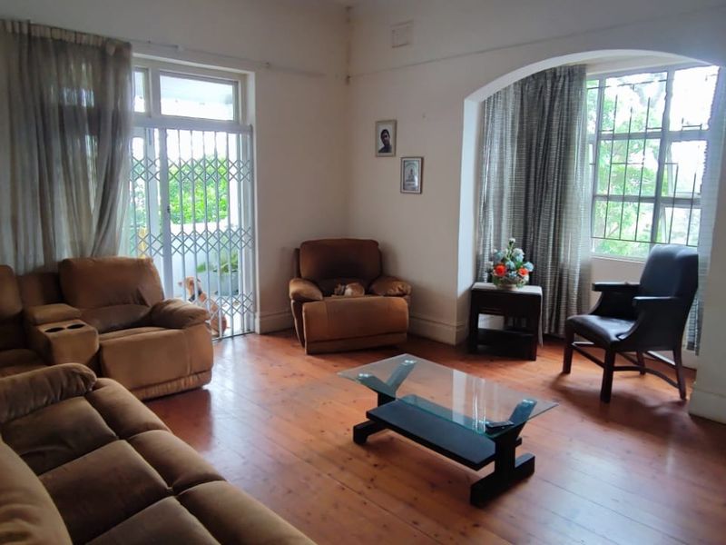 Spacious living room featuring original hardwood flooring, an arched window, and a fireplace mantel, offering a bright and comfortable living space.