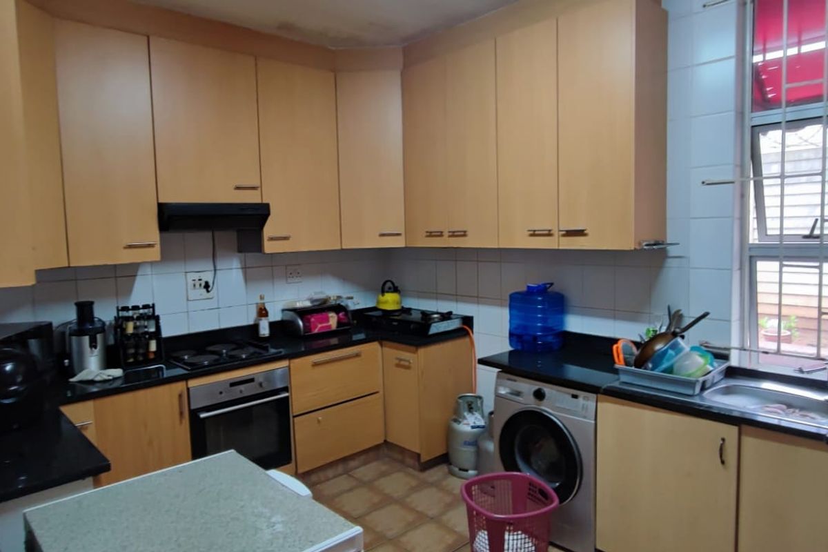 Functional kitchen featuring light wood cabinetry, black granite countertops, built-in oven, gas hob, and a double sink with security bars on the window.