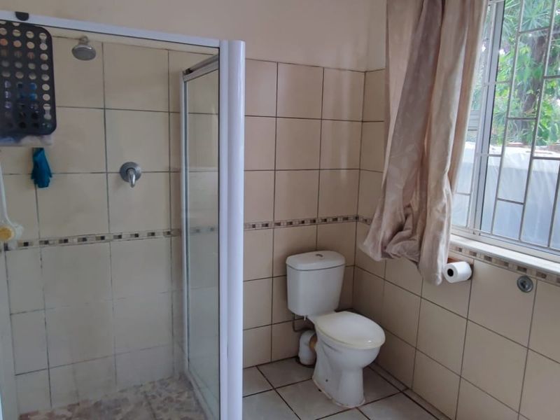 A functional bathroom featuring a shower enclosure, toilet, and tiled finishes, with a window providing natural light and security bars.