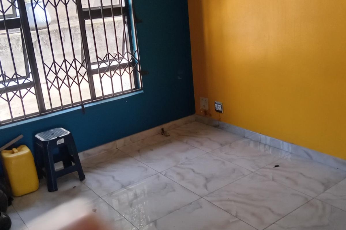 An empty bedroom featuring tiled flooring, security bars on the windows, and bold yellow and blue painted walls.