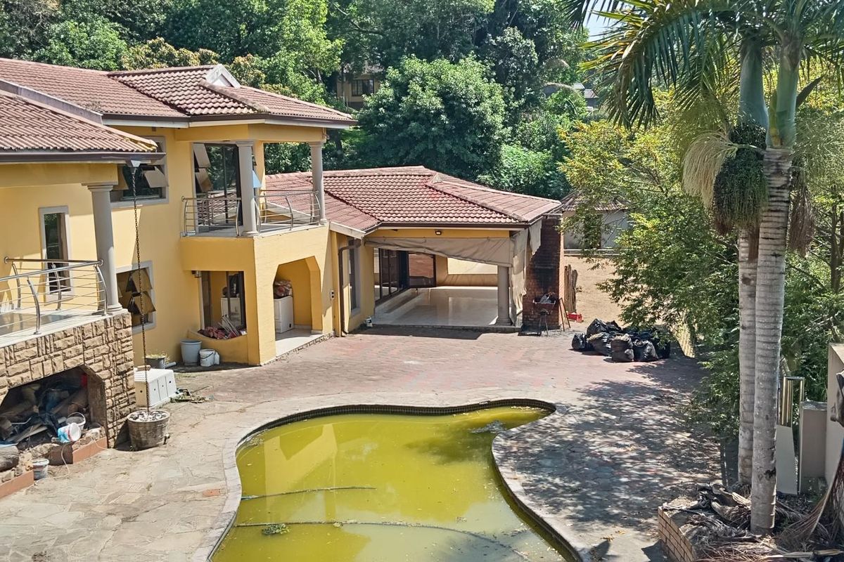 Rear exterior view of a multi-level house featuring a paved courtyard, covered patio, balcony with stainless steel railings, and a swimming pool requiring maintenance.
