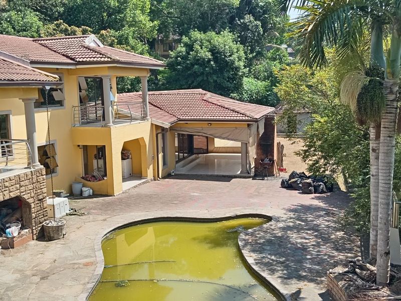 Rear exterior view of a multi-level house featuring a paved courtyard, covered patio, balcony with stainless steel railings, and a swimming pool requiring maintenance.