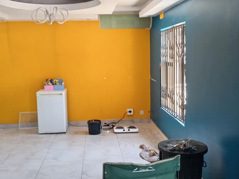 An open-plan living area featuring tiled floors, a decorative ceiling feature, and a structural column, currently requiring cosmetic updates and finishing touches.