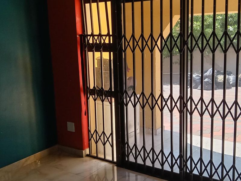 An empty living room featuring tiled flooring and a security gate leading to an outdoor patio area.