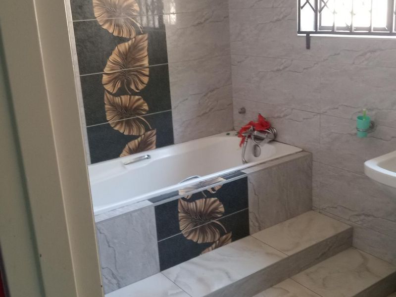 A functional bathroom featuring a built-in bathtub with decorative tile accents, a pedestal basin, and tiled wall finishes.