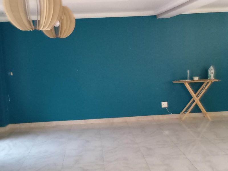 A spacious, empty living area featuring teal-painted walls, tiled flooring, and security bars on the window.