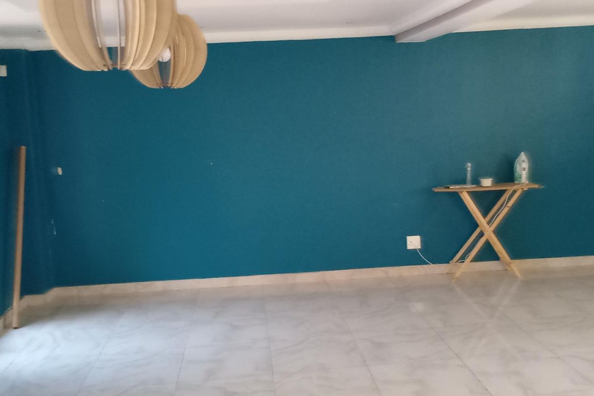 A spacious, empty living area featuring teal-painted walls, tiled flooring, and security bars on the window.