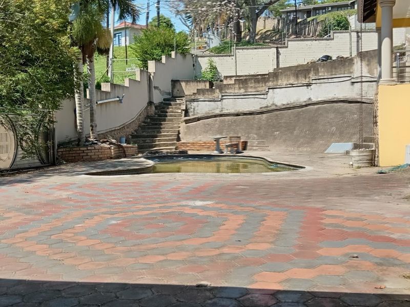 Outdoor pool area featuring a paved patio, tiered retaining walls, and concrete stairs, requiring maintenance and refurbishment to restore its appeal.