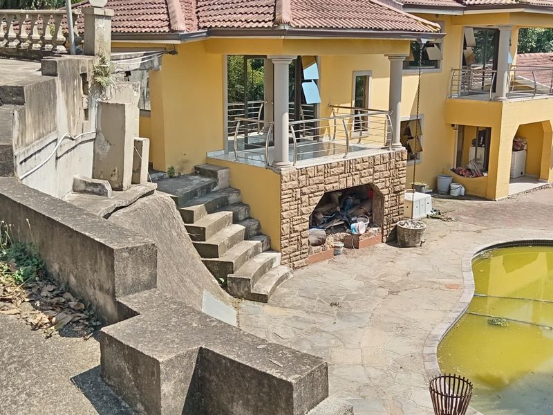 Rear exterior view featuring a swimming pool, paved patio area, and multi-level concrete retaining walls with stone-clad architectural details.