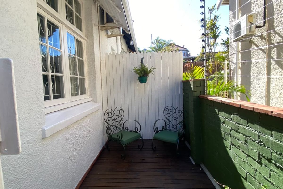 A compact outdoor patio area featuring timber decking, a painted brick boundary wall, and a privacy screen, suitable for a small seating arrangement.