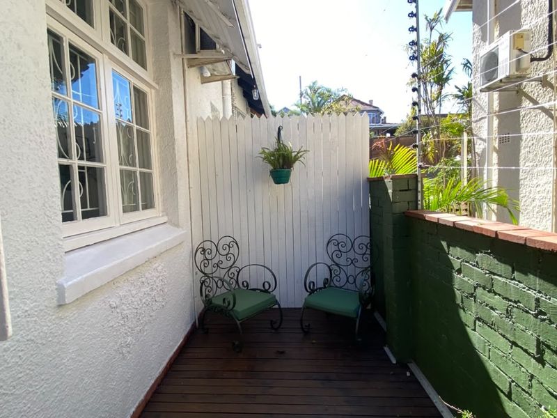 A compact outdoor patio area featuring timber decking, a painted brick boundary wall, and a privacy screen, suitable for a small seating arrangement.