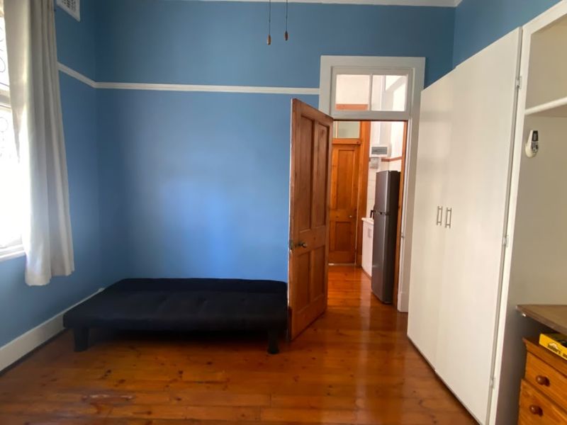 A bedroom featuring polished timber flooring, built-in wardrobe storage, and a classic transom window above the doorway.