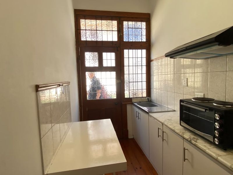 Compact kitchen featuring built-in cabinetry, stainless steel sink, tiled splashback, and an extractor fan, with direct access to the exterior via a timber door.