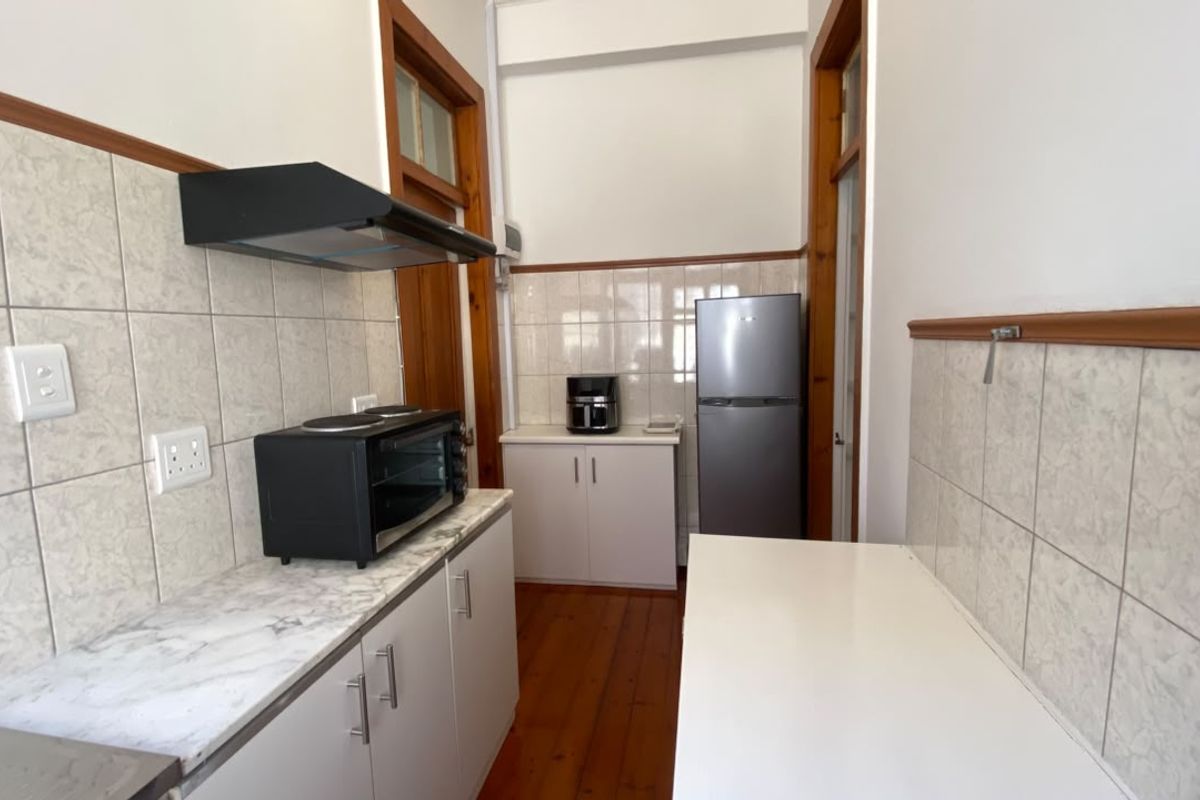 A functional kitchen featuring timber flooring, tiled splashbacks, laminate countertops, and built-in cabinetry with an integrated extractor fan.