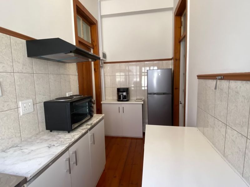 A functional kitchen featuring timber flooring, tiled splashbacks, laminate countertops, and built-in cabinetry with an integrated extractor fan.