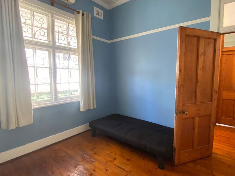 A bedroom featuring original timber flooring, decorative cornicing, picture rails, and a window with security grilles.
