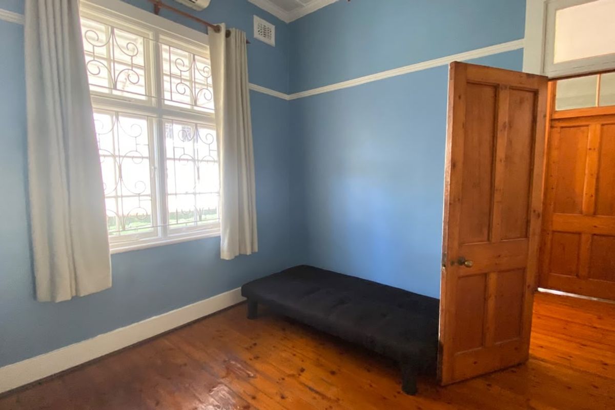 A bedroom featuring original timber flooring, decorative cornicing, picture rails, and a window with security grilles.