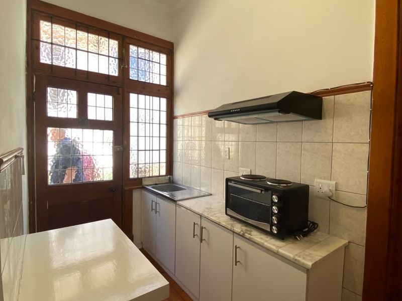 Compact kitchen featuring built-in cabinetry, stainless steel sink, extractor fan, and tiled splashback, with direct access through a character leaded glass door.