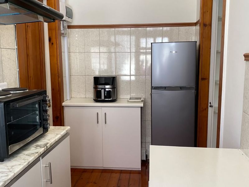 A functional kitchen area featuring tiled splashbacks, timber flooring, and built-in cabinetry with laminate countertops.