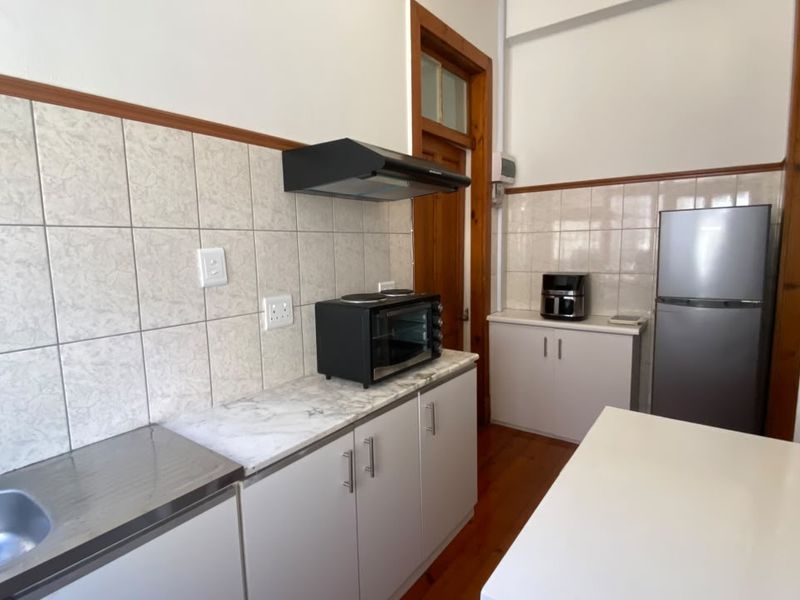 A functional kitchen featuring built-in cabinetry, a stainless steel sink, tiled backsplash, and timber flooring, providing a practical workspace within the cottage.