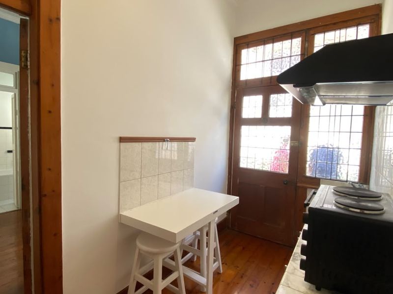 A compact kitchen area featuring timber flooring, a built-in extractor fan, and a classic timber door with leadlight glass detailing.
