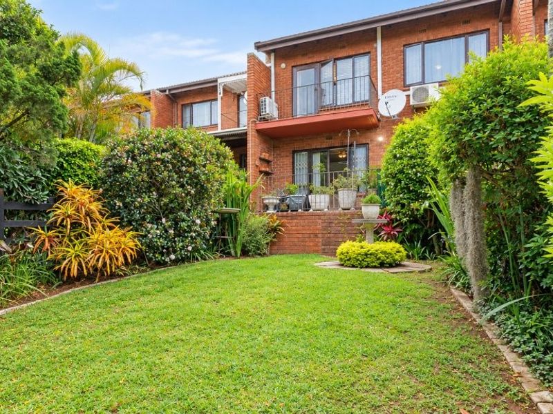 Rear view of a brick townhouse featuring a private garden, lawn, and an upper-level balcony.