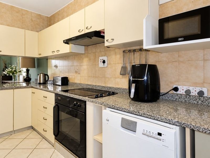 A functional kitchen featuring granite countertops, tiled backsplash, fitted cabinetry, and integrated appliances including an oven, hob, and extractor fan.