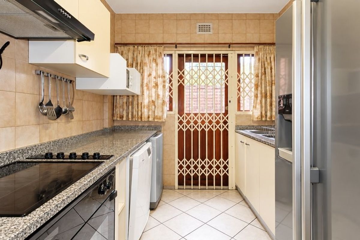 Functional kitchen featuring granite countertops, built-in oven, electric hob, extractor fan, and tiled finishes with direct access to the exterior via a security gate.
