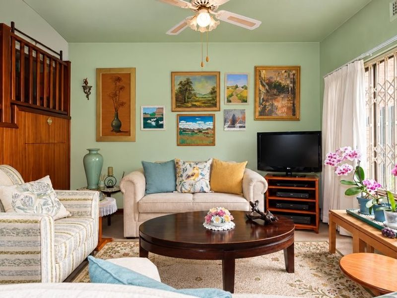 A cozy living room featuring a wooden staircase, ceiling fan, and large sliding glass doors with security gates leading to the exterior.