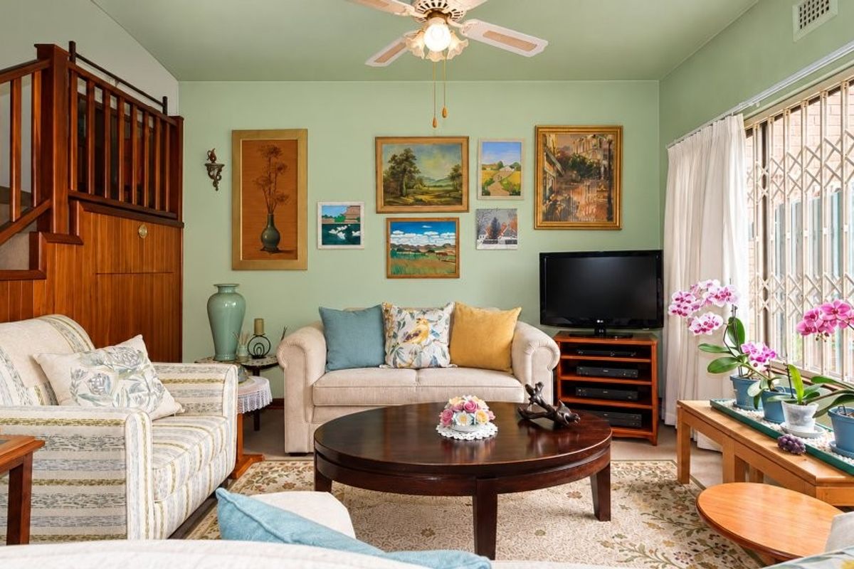 A cozy living room featuring a wooden staircase, ceiling fan, and large sliding glass doors with security gates leading to the exterior.