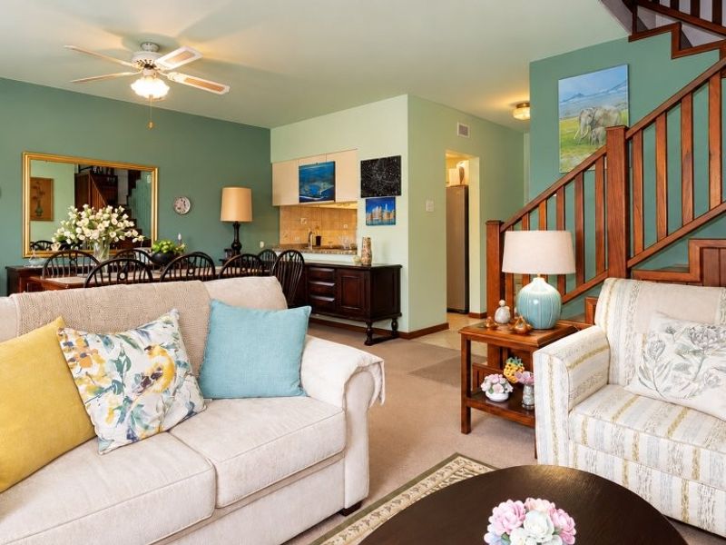 Open-plan living and dining area featuring a wooden staircase, ceiling fan, and integrated cabinetry, offering a functional and connected layout.