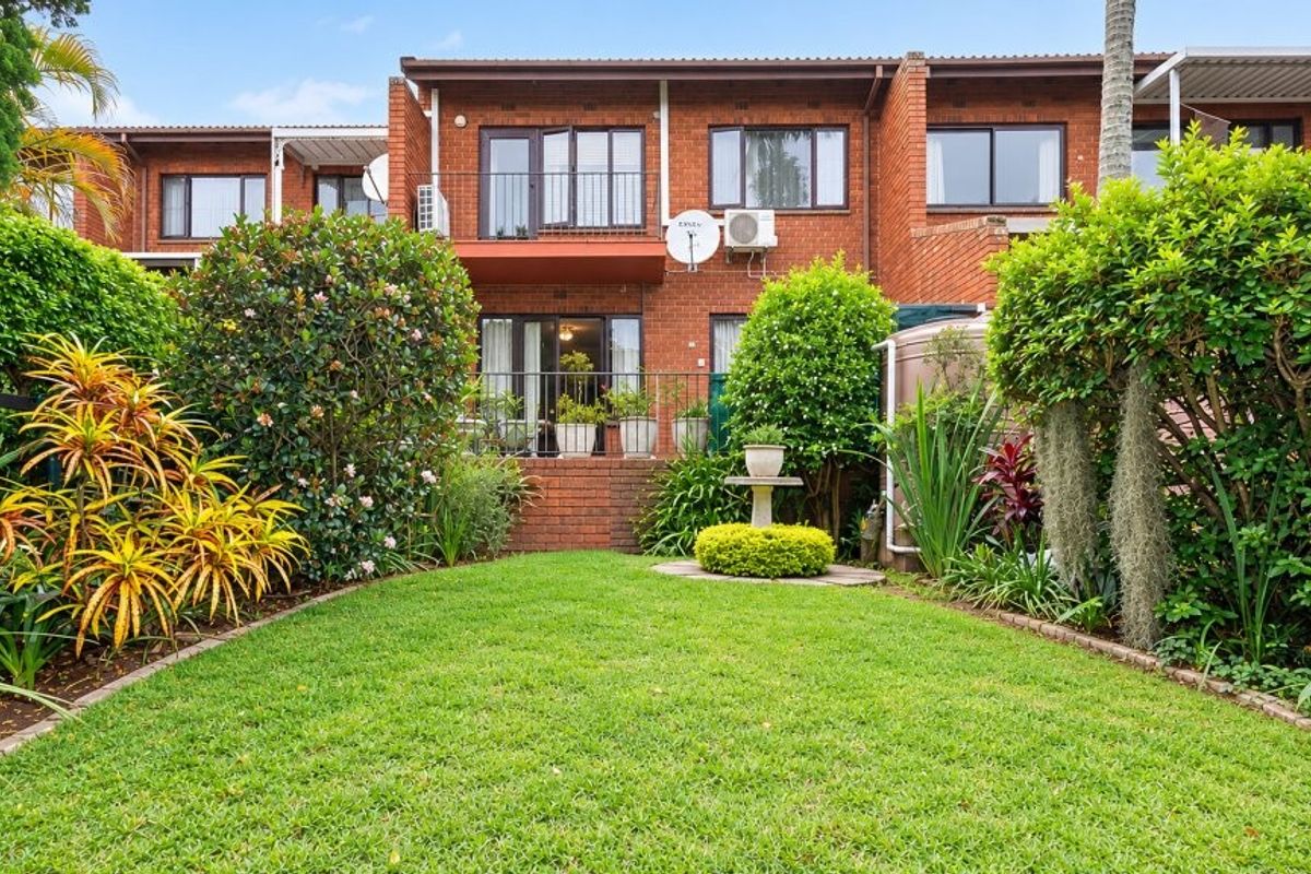 Rear view of a brick townhouse featuring a private garden, balcony, and established landscaping.