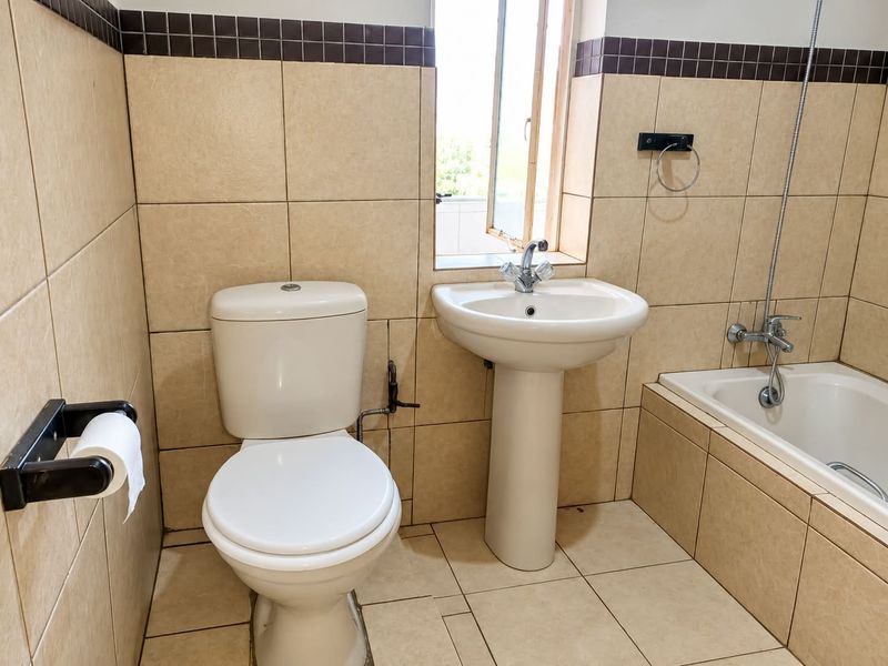 A functional bathroom featuring a pedestal washbasin, toilet, and bathtub with tiled walls and flooring, offering a clean and practical layout.