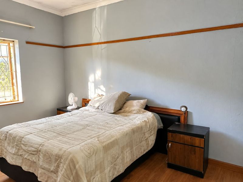 A bedroom featuring laminate flooring, a wooden picture rail, and a window with security bars, offering a functional space with potential for cosmetic updates.