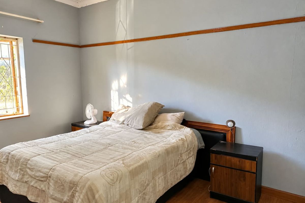 A bedroom featuring laminate flooring, a wooden picture rail, and a window with security bars, offering a functional space with potential for cosmetic updates.