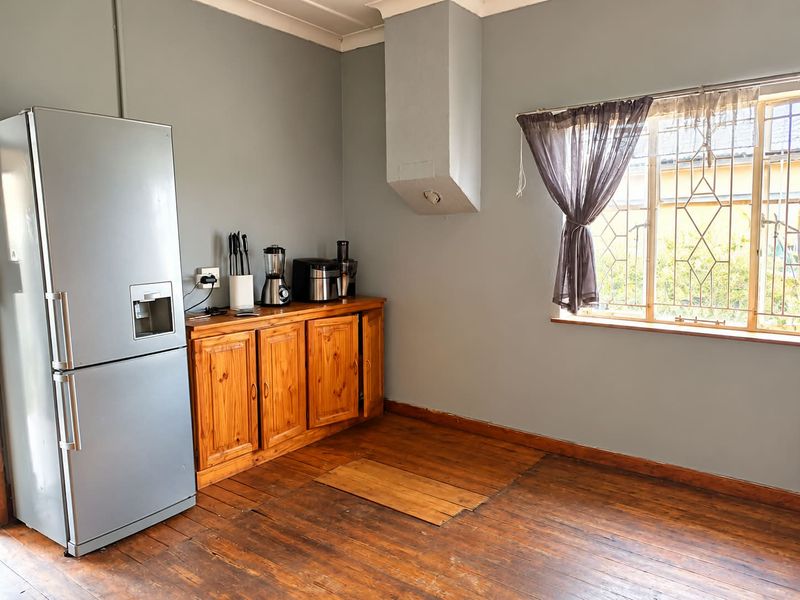 A kitchen area featuring timber cabinetry, wooden flooring, and a window with security bars, offering a functional space with potential for cosmetic updates.