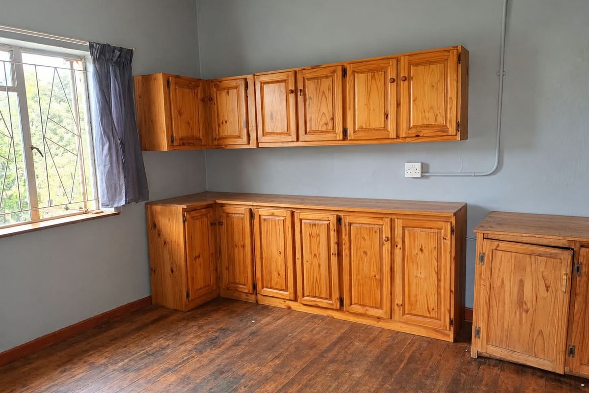 A functional kitchen area featuring wooden cabinetry, timber flooring, and security bars on the window, offering a blank canvas for renovation.