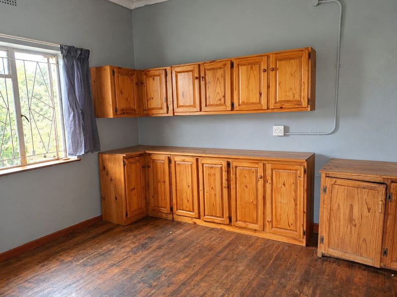 A functional kitchen area featuring wooden cabinetry, timber flooring, and security bars on the window, offering a blank canvas for renovation.