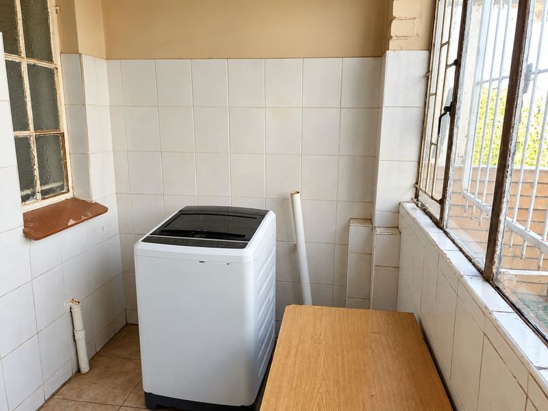 A functional laundry area featuring tiled walls and flooring, equipped with plumbing connections and security bars on the windows.