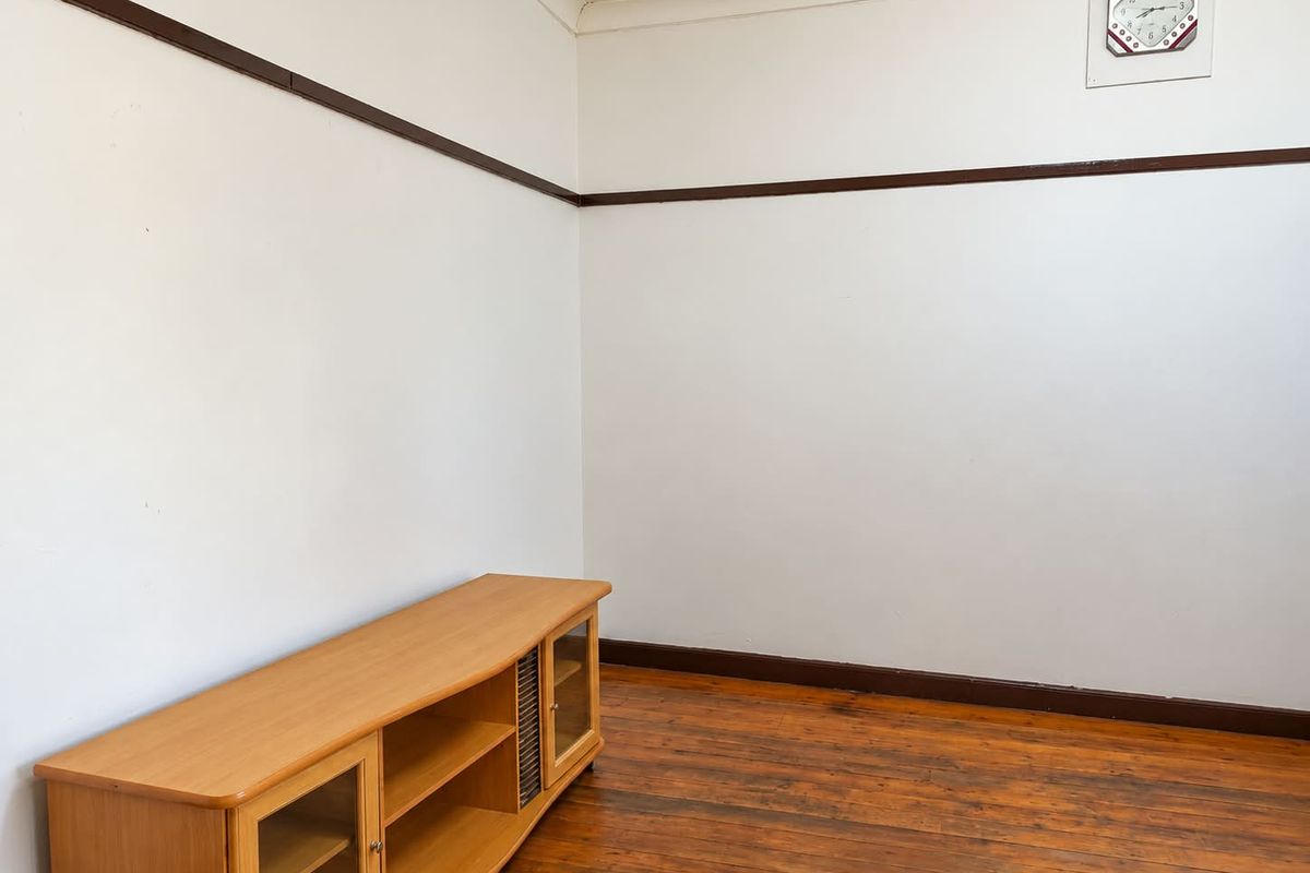 A simple living room featuring original timber flooring, white walls with dark timber picture rails, and classic skirting boards.