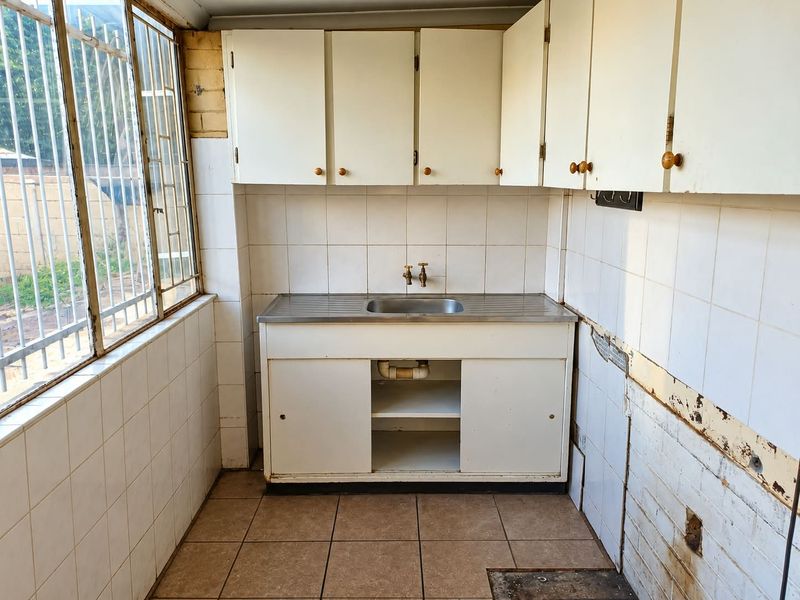 A functional scullery or utility area featuring a stainless steel sink, built-in cabinetry, and tiled finishes, currently requiring cosmetic renovation and repair.