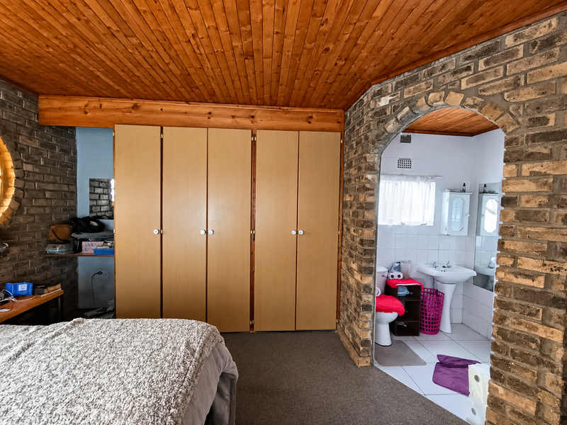 Bedroom featuring exposed brick walls, timber ceiling, and built-in cupboards, with an open-plan en-suite bathroom containing a pedestal basin and toilet.