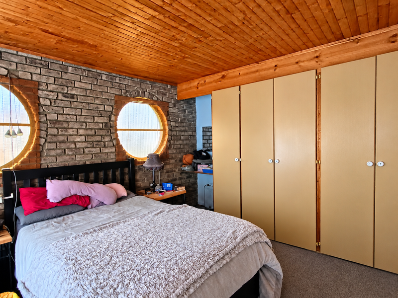 Bedroom featuring a distinctive exposed brick wall, circular windows, and a warm timber ceiling with ample built-in wardrobe storage.