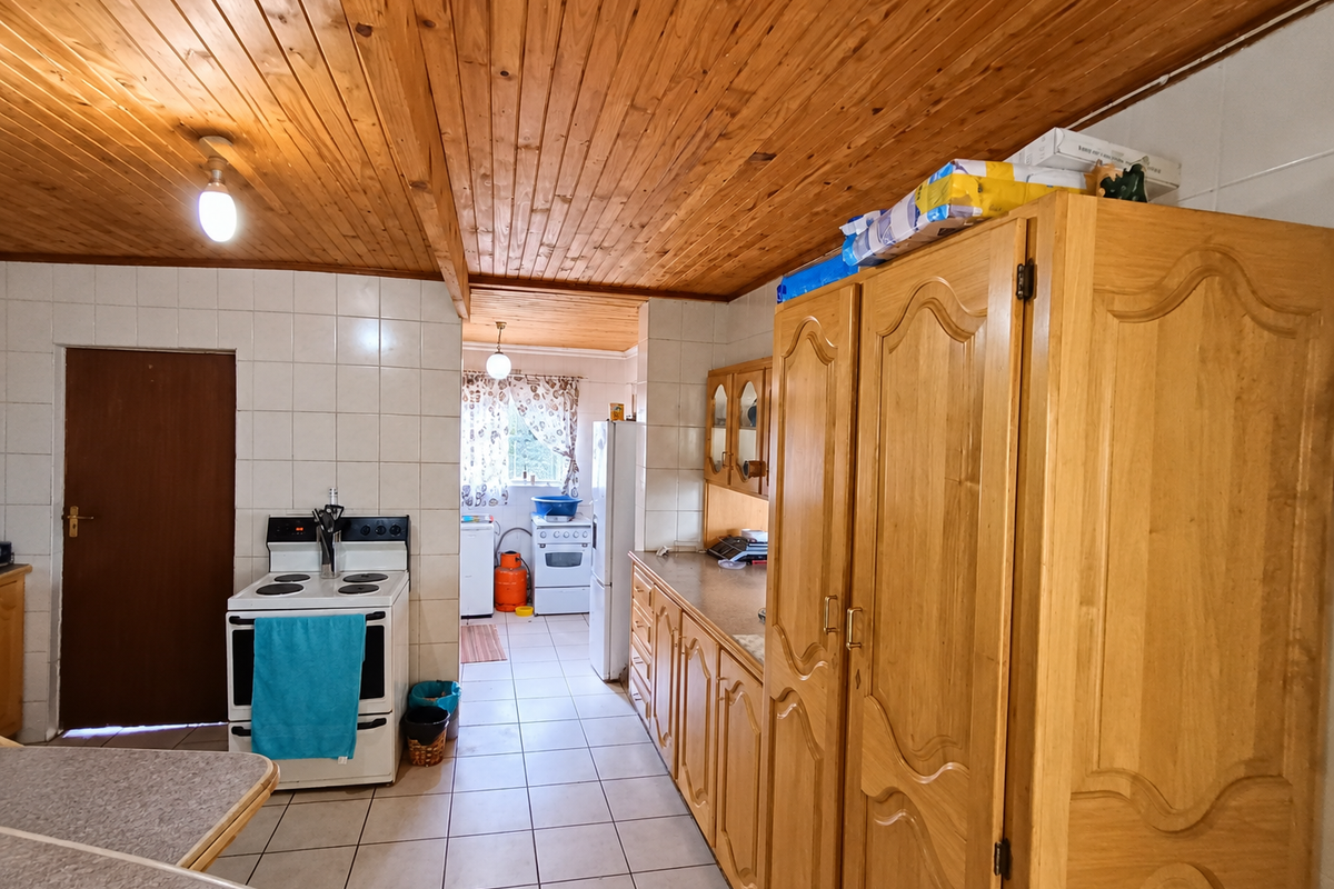 A dated kitchen featuring timber tongue and groove ceilings, tiled flooring, and traditional wooden cabinetry with a freestanding stove.