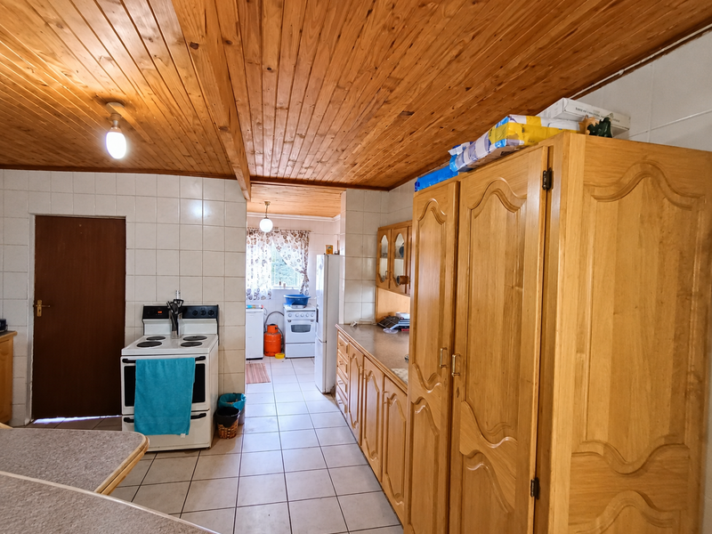 A dated kitchen featuring timber tongue and groove ceilings, tiled flooring, and traditional wooden cabinetry with a freestanding stove.